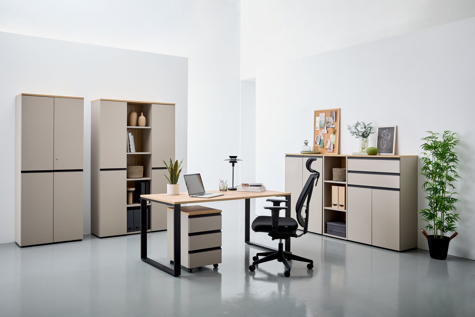 Moderne Büromöbel in einem hellen Raum, bestehend aus einem Winkelschreibtisch mit Rollcontainer, einem ergonomischen Bürostuhl und mehreren Aktenschränken. Perspektive von vorne.