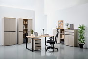 Moderne Büromöbel in einem hellen Raum, bestehend aus einem Winkelschreibtisch mit Rollcontainer, einem ergonomischen Bürostuhl und mehreren Aktenschränken. Perspektive von vorne.
