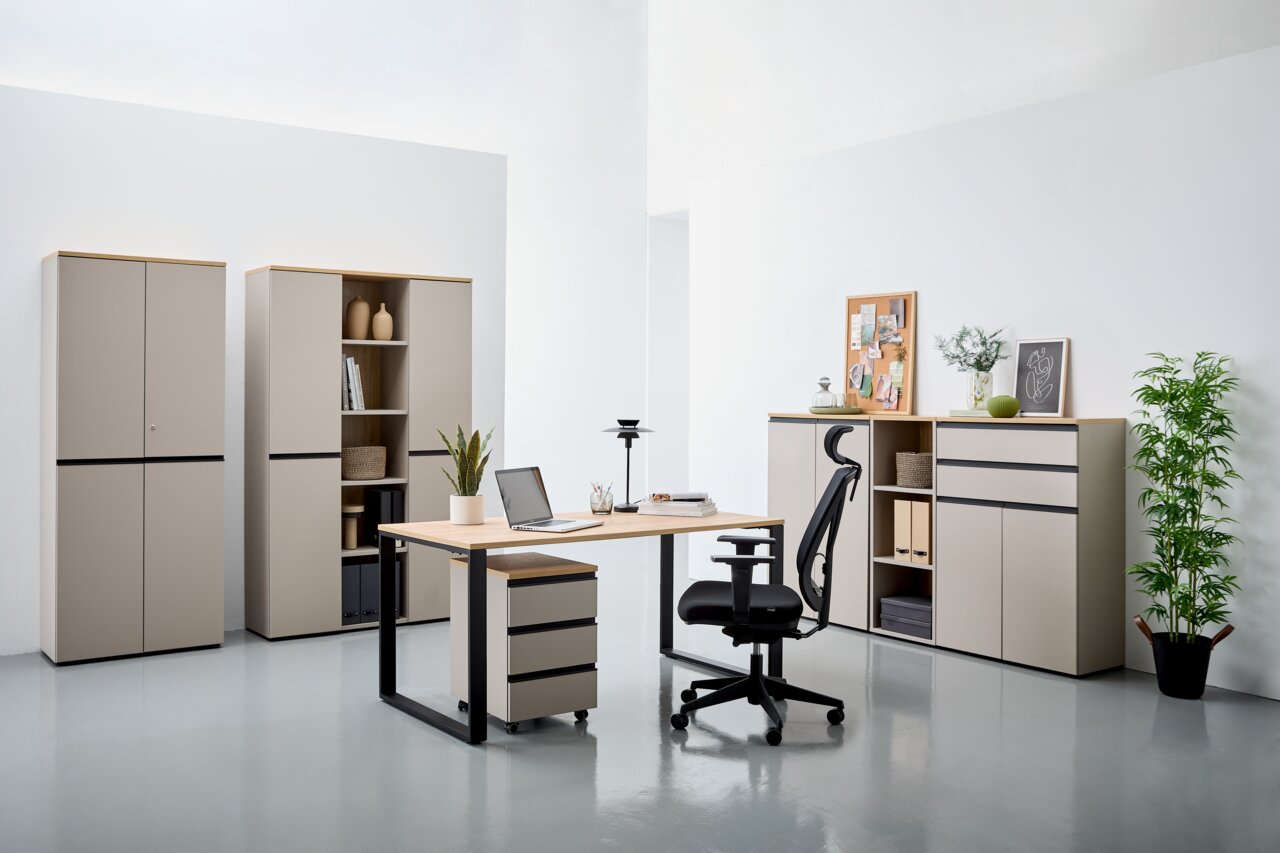 Moderne Büromöbel in einem hellen Raum, bestehend aus einem Winkelschreibtisch mit Rollcontainer, einem ergonomischen Bürostuhl und mehreren Aktenschränken. Perspektive von vorne.