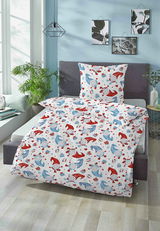 Biber Bettwäsche 100x135cm mit buntem Muster aus roten und blauen Mützen und Geschenken, auf einem Bett in einem hellen Raum mit Pflanzen und Wanddekorationen, aus der Perspektive von vorne fotografiert.