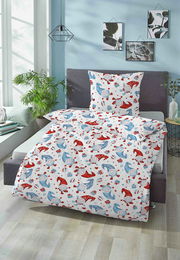 Biber Bettwäsche 100x135cm mit buntem Muster aus roten und blauen Mützen und Geschenken, auf einem Bett in einem hellen Raum mit Pflanzen und Wanddekorationen, aus der Perspektive von vorne fotografiert.