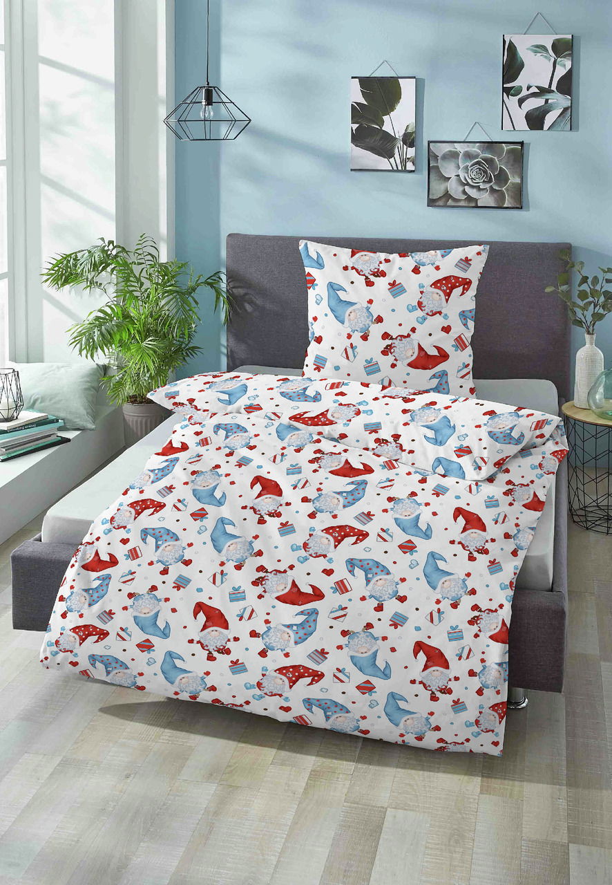 Biber Bettwäsche 100x135cm mit buntem Muster aus roten und blauen Mützen und Geschenken, auf einem Bett in einem hellen Raum mit Pflanzen und Wanddekorationen, aus der Perspektive von vorne fotografiert.