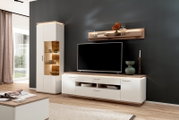 Moderne Wohnzimmer-Wohnwand in Weiß und Holzoptik mit TV-Lowboard, beleuchtetem Vitrinenschrank und Wandregal vor dunkler Wand, Ansicht schräg von vorn