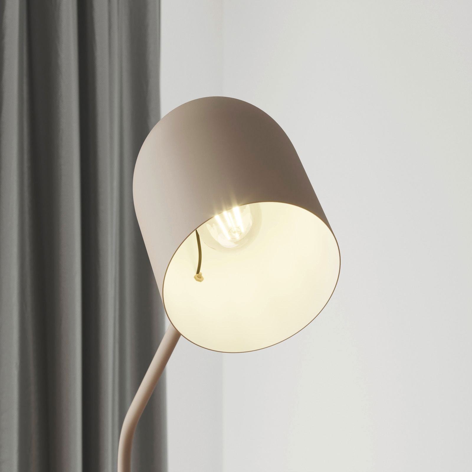 Nahaufnahme einer modernen Stehleuchte mit einem schlichten, runden Lampenschirm in Beige, der eine Glühbirne umgibt. Die Perspektive zeigt die Leuchte von der Seite, mit einem grauen Vorhang im Hintergrund.
