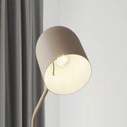 Nahaufnahme einer modernen Stehleuchte mit einem schlichten, runden Lampenschirm in Beige, der eine Glühbirne umgibt. Die Perspektive zeigt die Leuchte von der Seite, mit einem grauen Vorhang im Hintergrund.