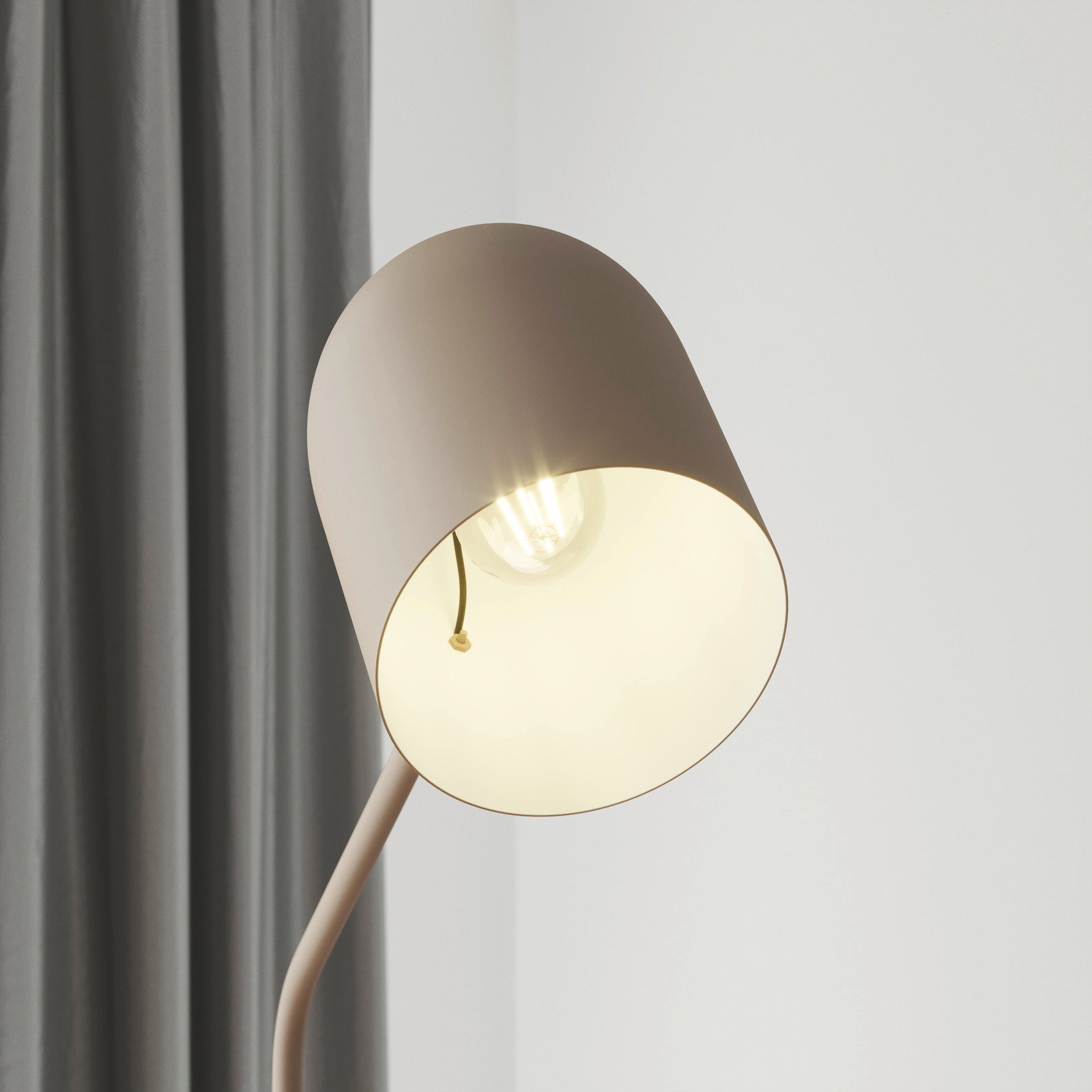 Nahaufnahme einer modernen Stehleuchte mit einem schlichten, runden Lampenschirm in Beige, der eine Glühbirne umgibt. Die Perspektive zeigt die Leuchte von der Seite, mit einem grauen Vorhang im Hintergrund.