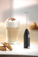 Milchaufschäumer Fino in Seitenansicht neben einem Glas Latte Macchiato und Gebäck.