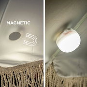 Nahaufnahme aus leicht seitlicher Perspektive: runde, magnetische LED-Zeltlampe in Weiß, an der Innenwand eines Zelts befestigt, mit sichtbarem Magnet-Symbol und Stoffstruktur.