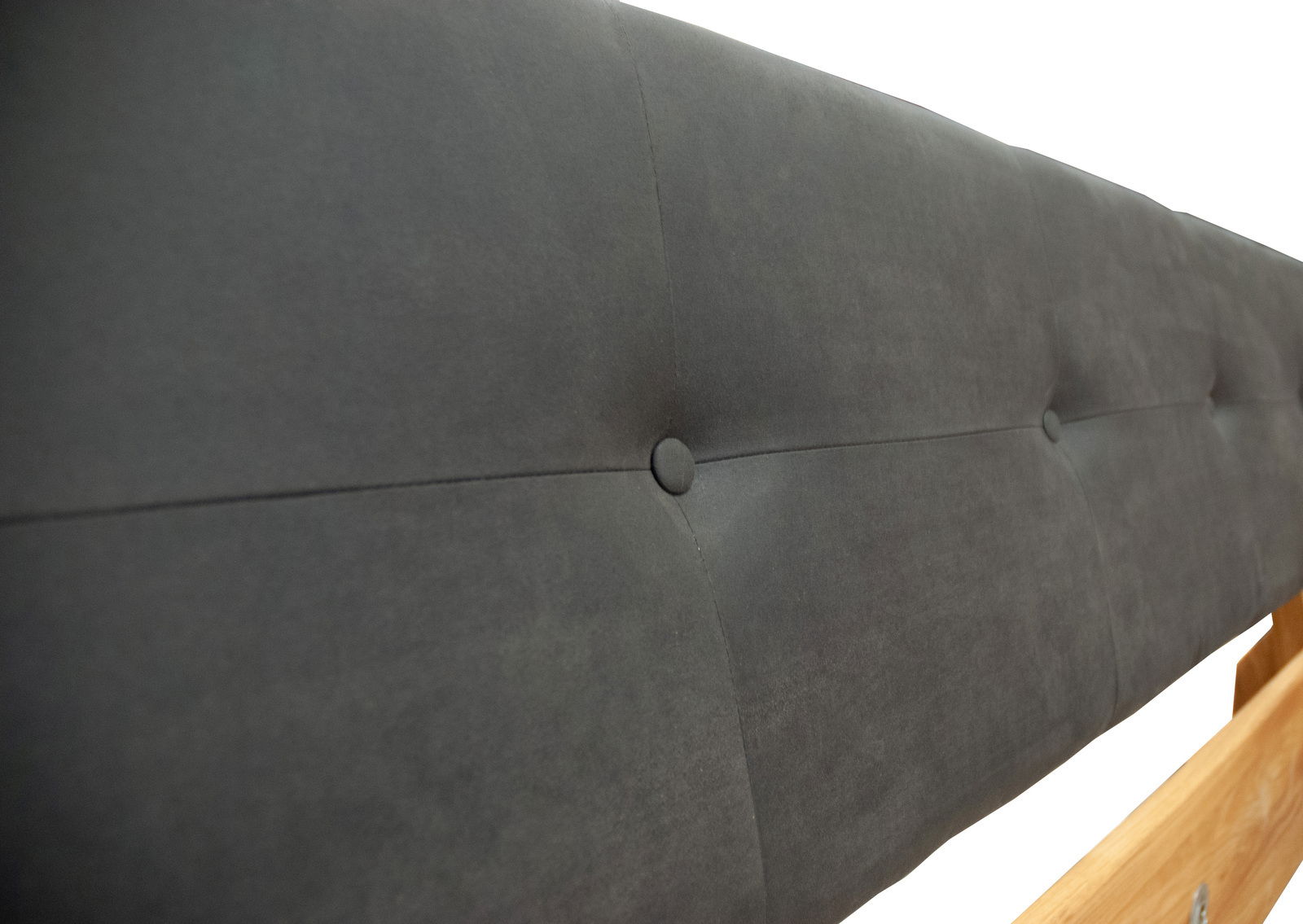 Nahaufnahme eines gepolsterten, dunkelgrauen Betthauptes mit Knopfdetails, seitliche Perspektive