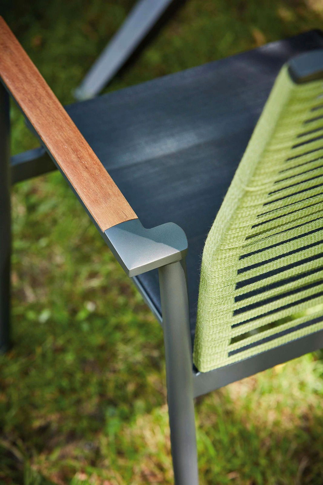 Nahaufnahme eines Sessels mit Holzarmlehne und grünem, geflochtenem Sitz, von oben betrachtet.