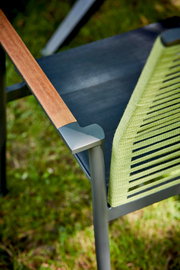 Nahaufnahme eines Sessels mit Holzarmlehne und grünem, geflochtenem Sitz, von oben betrachtet.