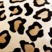 Close-up van een sierkussen met luipaardprint in beige, zwart en bruin.