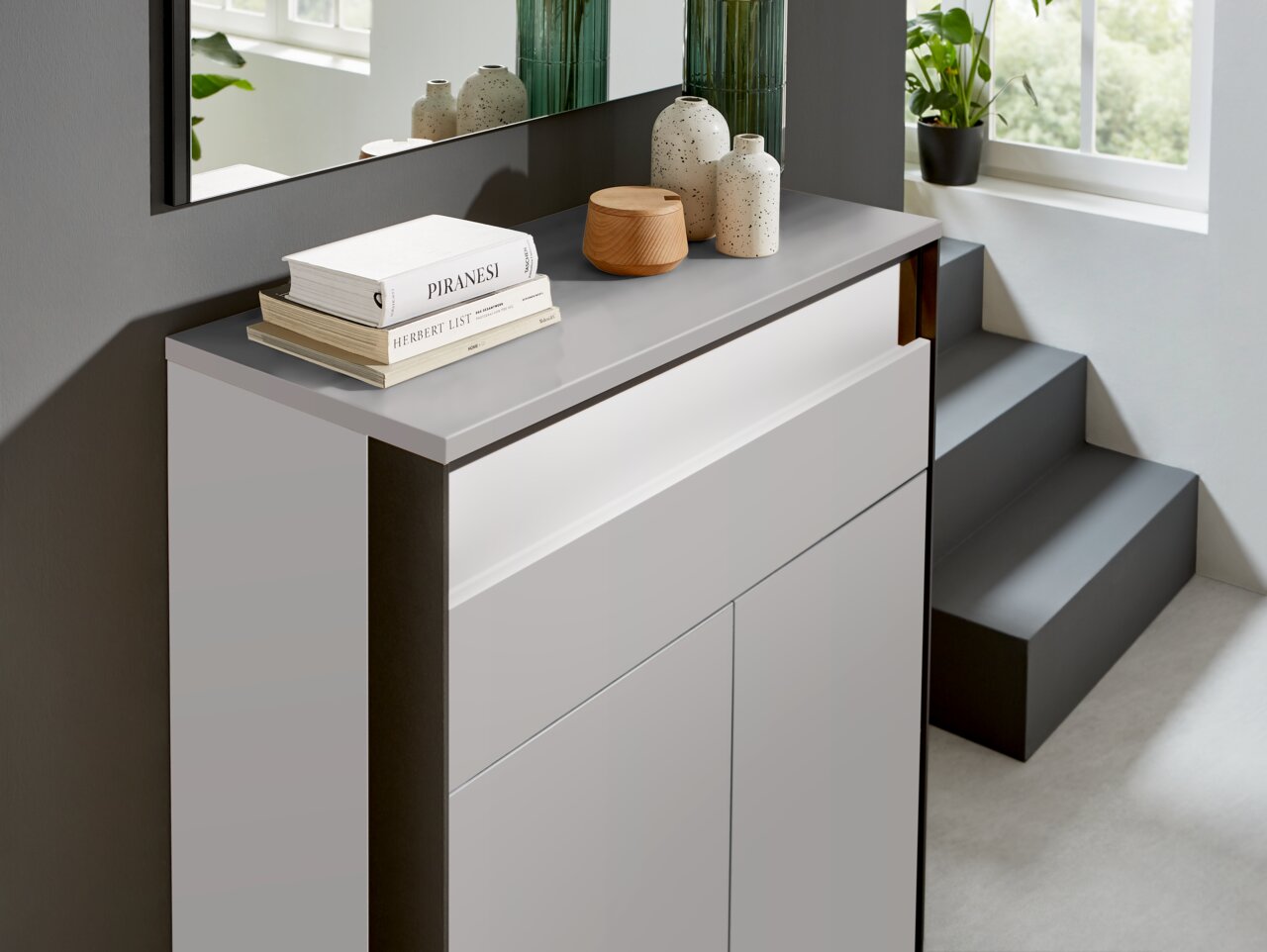 Moderner Schuhschrank in hellem Raum, seitliche Perspektive, dekoriert mit Büchern und Vasen.