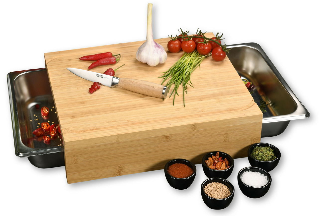 Schneidebrett aus Holz mit zwei Edelstahl-Auffangschalen, darauf liegen ein Messer, Knoblauch, Tomaten und Kräuter. Perspektive von vorne.