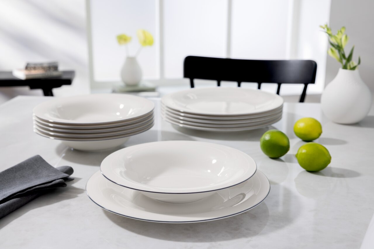 Elegantes Tafelservice 12-teilig in Weiß mit dezentem Rand, auf einem Tisch arrangiert, seitliche Perspektive.