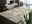 OCI Designer Teppich BESTSELLER Designer Teppich in einem modernen Wohnzimmer mit dunklem Holzboden, Kamin und grünen Dekorationsobjekten, aus einer seitlichen Perspektive fotografiert.