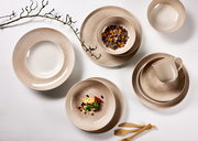 Vogelperspektive auf ein elegantes Geschirrset in Beige- und Brauntönen, bestehend aus Tellern, Schalen und einer Tasse, dekoriert mit Zweigen und Holzbesteck.