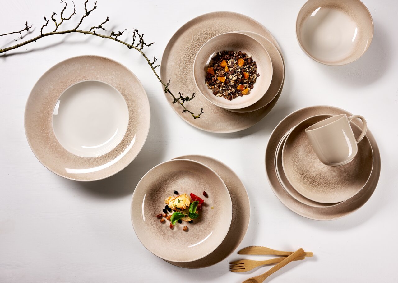 Een vogelperspectief op een elegant servies in beige- en bruintinten, bestaande uit borden, schalen en een kopje, versierd met takjes en houten bestek.