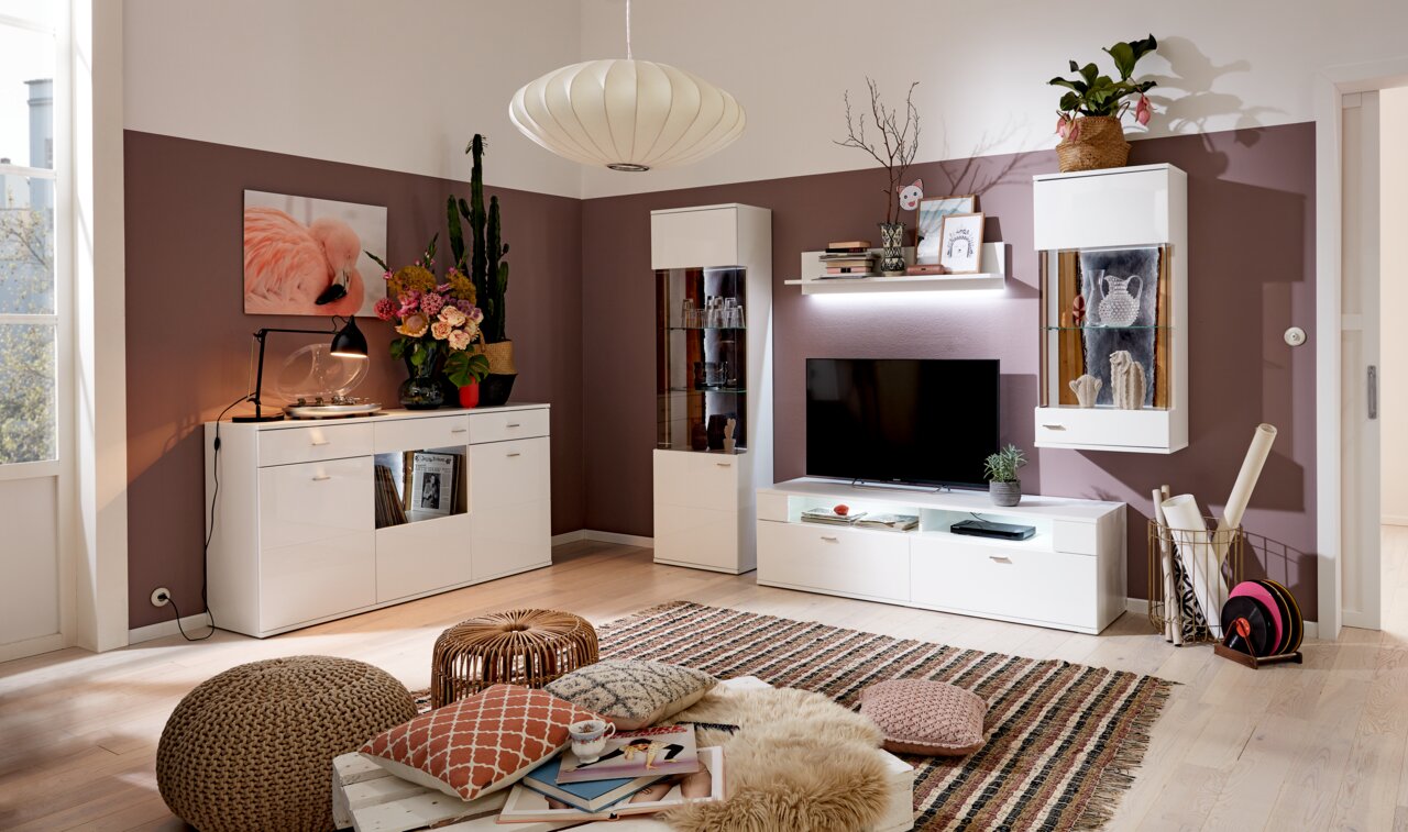 Wohnzimmer mit modernem TV-Aufsatz in Weiß, umgeben von stilvollen Regalen und Dekorationen, aus der Perspektive des Raumes betrachtet.