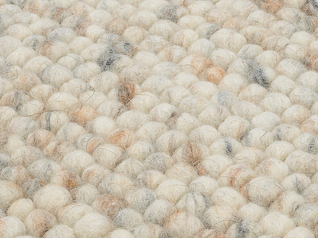 Nahaufnahme eines handgewebten Teppichs mit einer strukturierten, wolligen Oberfläche in natürlichen Creme- und Beigetönen.