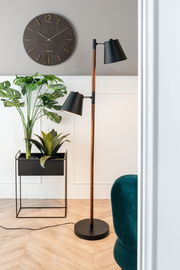 Modernes Wohnzimmer mit einer Stehlampe, einem Pflanzgefäß-Set mit grünen Pflanzen und einer Wanduhr. Perspektive von der Seite.