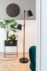 Modernes Wohnzimmer mit einer Stehlampe, einem Pflanzgefäß-Set mit grünen Pflanzen und einer Wanduhr. Perspektive von der Seite.