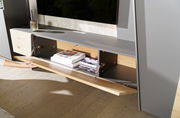 Nahaufnahme einer modernen Wohnwand mit grauer Oberfläche und Holzdetails, offene Klappe zeigt Stauraum mit Büchern.