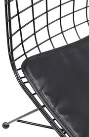 Nahaufnahme eines modernen Stuhls mit schwarzem Drahtgestell und gepolstertem Sitzkissen, seitliche Perspektive