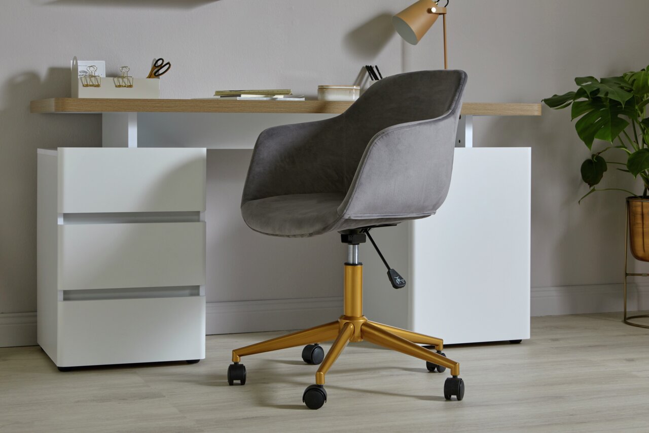 Grijze bureaustoel met gouden poten en wieltjes, gezien vanaf de zijkant, voor een modern bureau met witte lades.