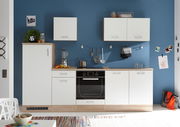 Moderne Küchenzeile mit weißen Schränken und Holzarbeitsplatte, frontal fotografiert vor einer blauen Wand.