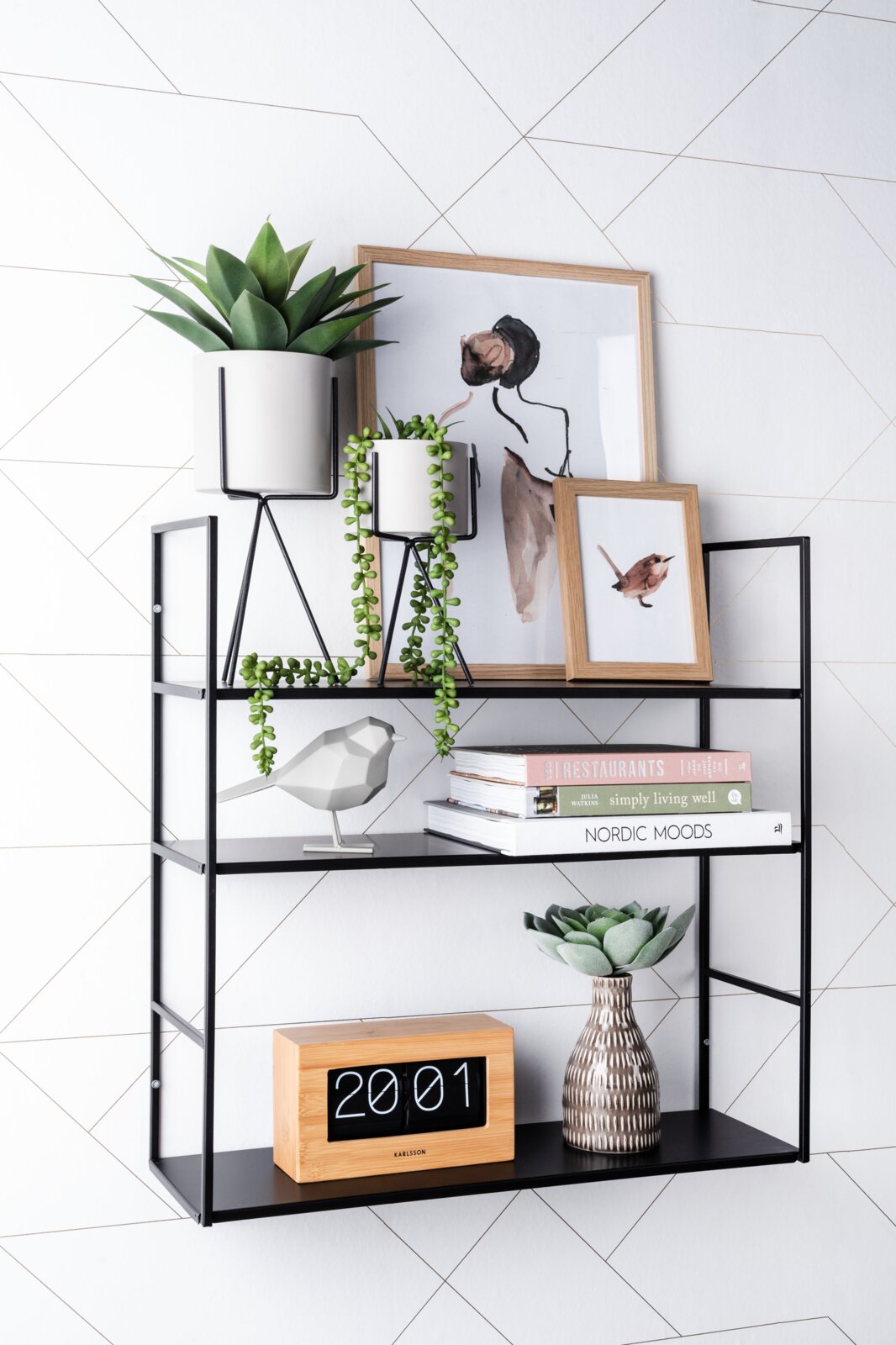 Moderne wandplank van zwart metaal met decoraties zoals planten, boeken en foto’s, gezien vanaf de zijkant.