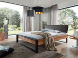 Modernes Balkenbett aus Holz mit schwarzem Metallrahmen, seitliche Perspektive, in einem hellen Raum mit großen Fenstern und stilvoller Dekoration.