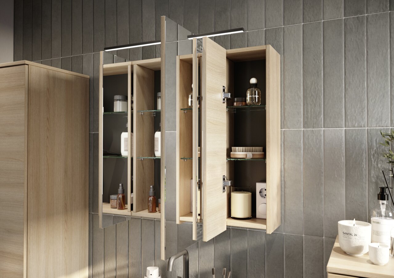 Geöffneter Spiegelschrank aus Holz mit Glasregalen, gefüllt mit Pflegeprodukten, aus seitlicher Perspektive fotografiert.