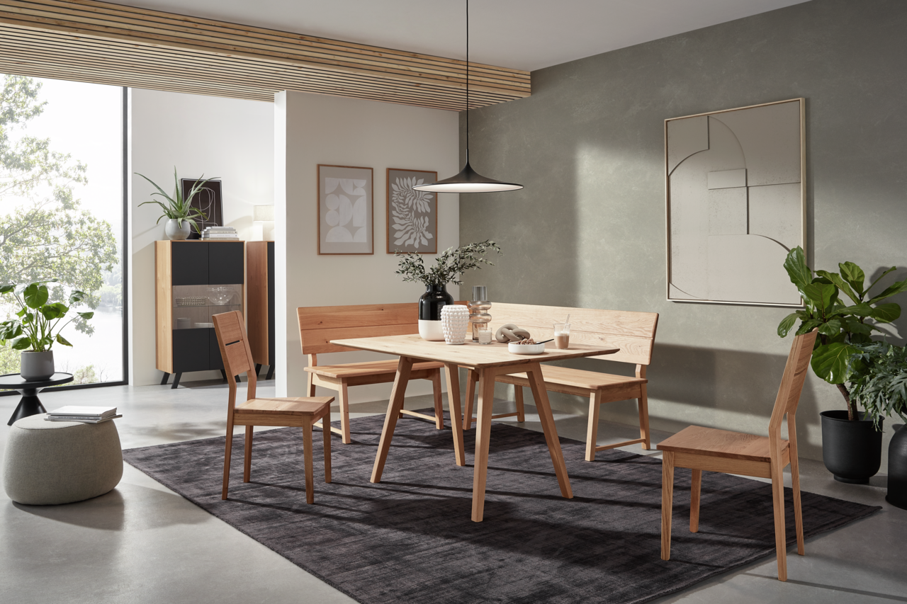 Valnatura Esstisch LARINO Moderne Esszimmer-Einrichtung mit Holztisch, Eckbank und Stühlen in einem hellen Raum mit Pflanzen und Wanddekorationen, seitliche Perspektive.