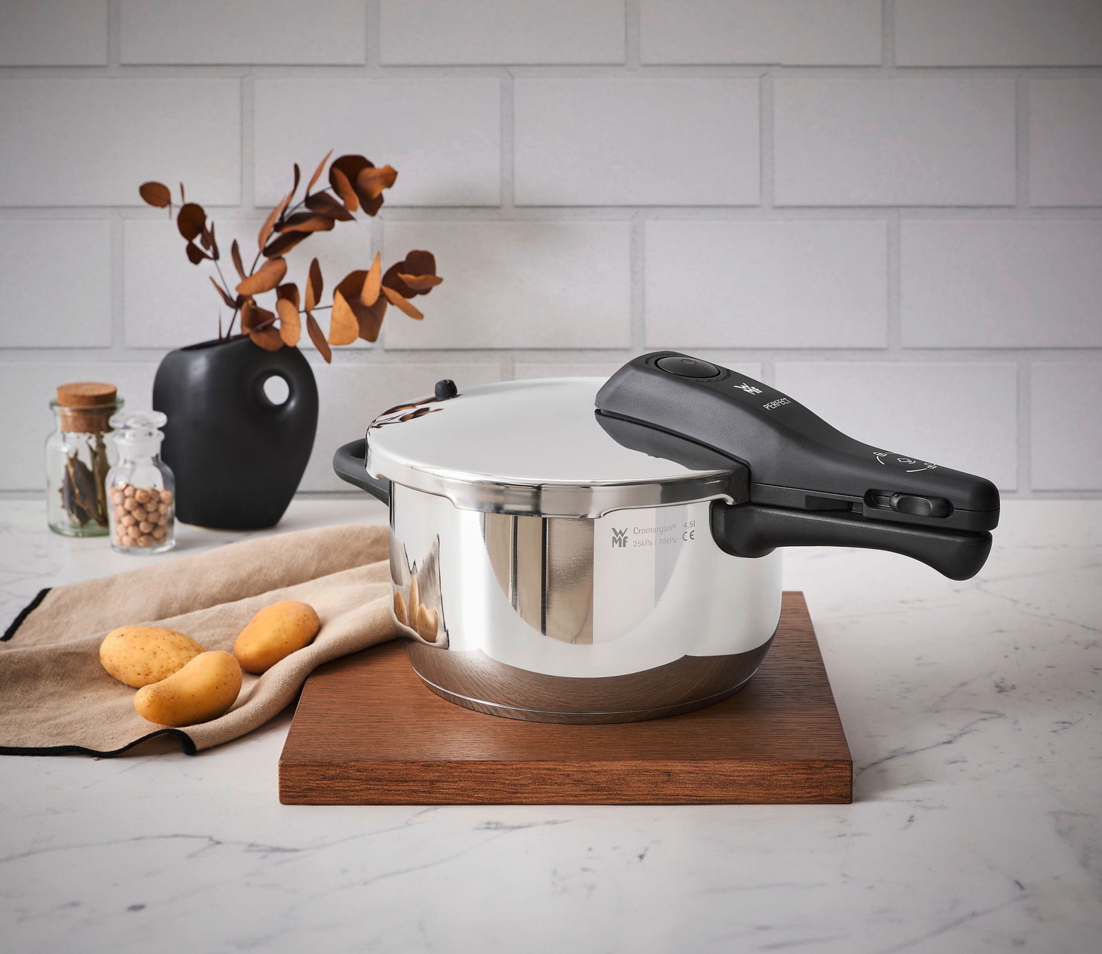 Schnellkochtopf WMF Perfect Neu 4,5L, seitliche Perspektive, auf Holzbrett in moderner Küchenszene mit Kartoffeln und Dekoration.