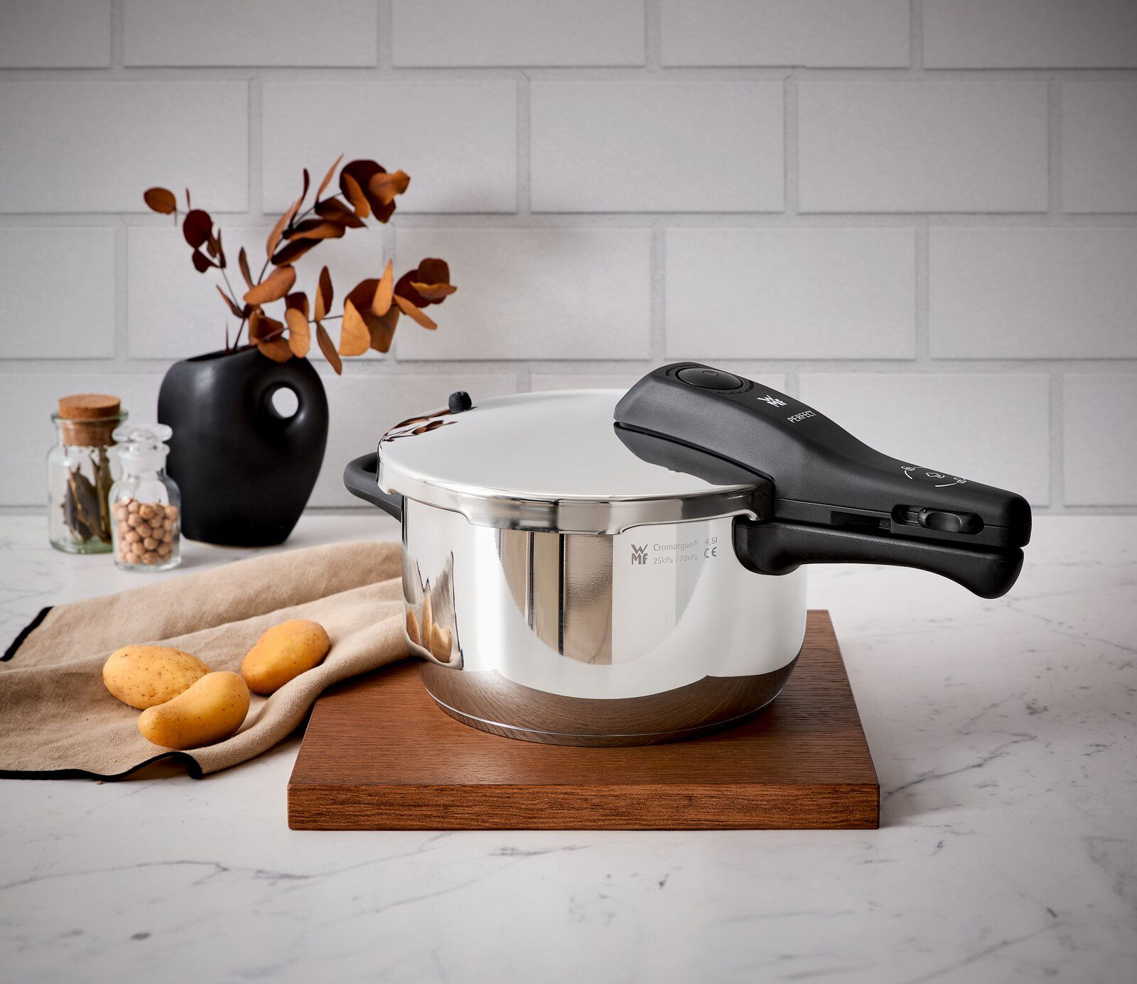 Schnellkochtopf WMF Perfect Neu 4,5L, seitliche Perspektive, auf Holzbrett in moderner Küchenszene mit Kartoffeln und Dekoration.