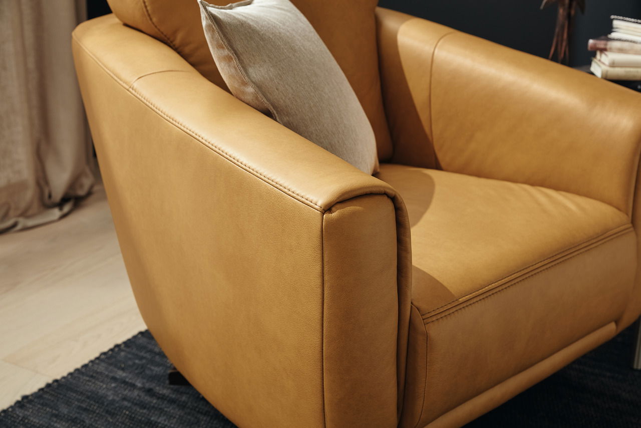 Nahaufnahme eines eleganten, senffarbenen Ledersessels mit Kissen, seitliche Perspektive