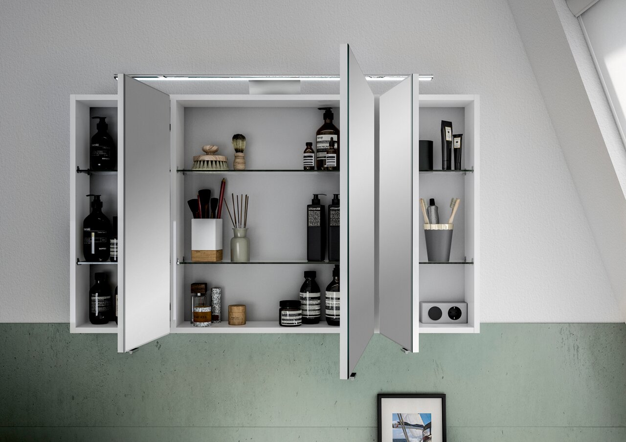 Spiegelschrank mit geöffneten Türen, gefüllt mit Pflegeprodukten und Accessoires, aus der Frontalperspektive fotografiert.