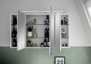 Spiegelschrank mit geöffneten Türen, gefüllt mit Pflegeprodukten und Accessoires, aus der Frontalperspektive fotografiert.