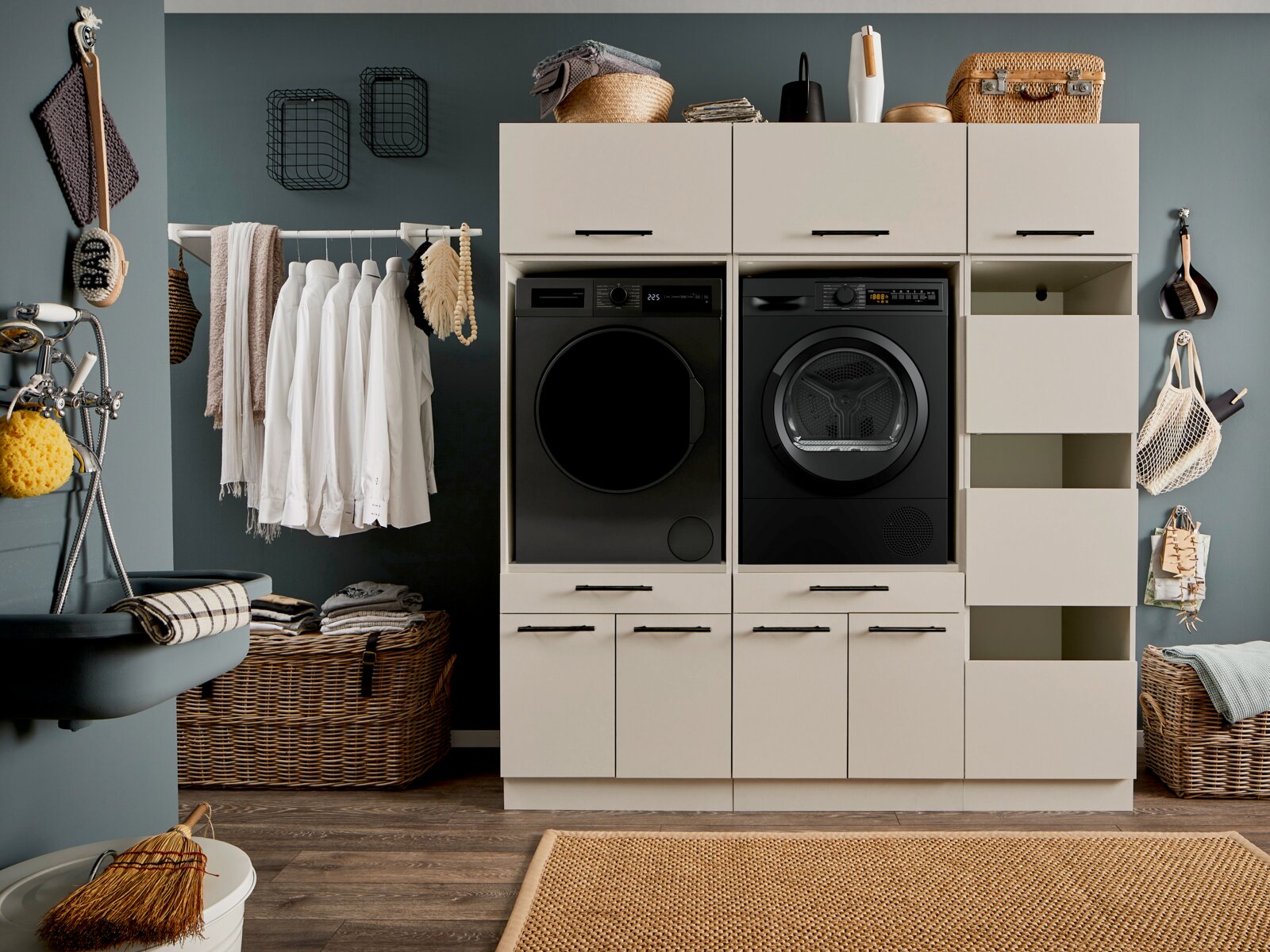 XORA Hauswirtschaftsraum-Kombi PRIMUS Moderne Waschküche mit weißem Waschmaschinen- und Trocknerschrank, schwarzer Frontlader-Waschmaschine und schwarzem Wäschetrockner sowie offenen Regalfächern und Schubladen, frontal aus Augenhöhe fotografiert.