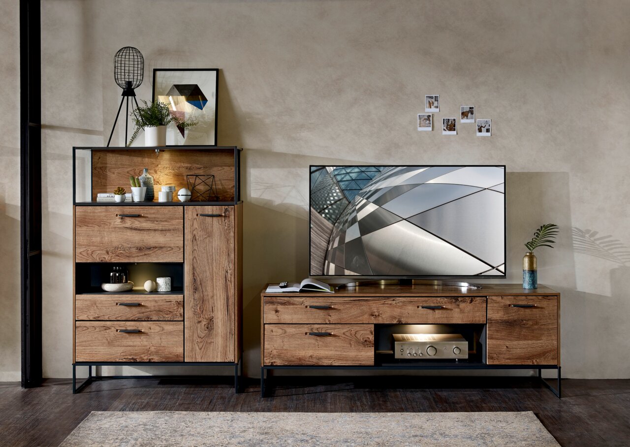 Wohnzimmeransicht mit moderner Wandkombination aus Holz und Metall, bestehend aus einem hohen Schrank mit Dekoration und einem TV-Unterteil mit Flachbildfernseher, von vorne betrachtet.