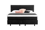 Boxspringbed met donkere stoffen bekleding en hoofdeinde, versierd met kussens, vooraanzicht