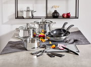 Kochtopf-Starter-Set 10-tlg. aus Edelstahl, bestehend aus mehreren Töpfen und Pfannen mit Glasdeckeln, Küchenutensilien und Schneidebrett, auf einer Küchenarbeitsplatte von vorne fotografiert.