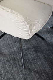 Nahaufnahme eines cremefarbenen Armlehnstuhls mit geripptem Stoffbezug und schwarzen Metallbeinen, von oben betrachtet.