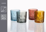 Vier Whiskygläser in verschiedenen Farben (blau, grau, rot, gelb) mit facettiertem Design, auf einer reflektierenden Oberfläche aus seitlicher Perspektive.