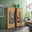 Zwei moderne Highboards aus Holz mit Glaseinsätzen, dekoriert mit Vasen und Geschirr, in einem stilvollen Wohnzimmer mit grüner Wand und großem Fenster, seitliche Perspektive.