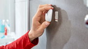 Hand befestigt einen weißen Haken mit tesa Powerstrips an einer Badezimmerwand, seitliche Perspektive