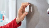 Hand befestigt einen weißen Haken mit tesa Powerstrips an einer Badezimmerwand, seitliche Perspektive