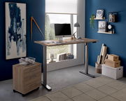 Moderner höhenverstellbarer E-Schreibtisch in einem stilvollen Büro mit blauer Wand, seitlicher Perspektive.