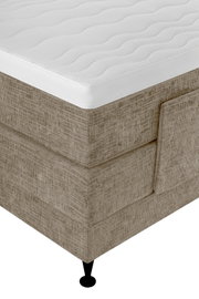 Nahaufnahme aus schräger Vogelperspektive auf ein beigefarbenes Boxspringbett mit weißer, weich gesteppter Matratzenauflage und schwarzem Fuß